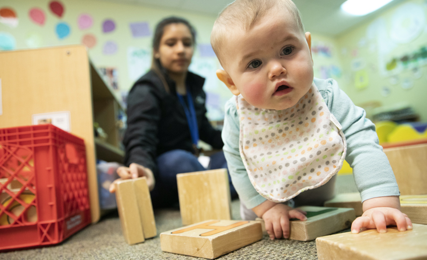 Toddler plays with blocks as child care provider looks on