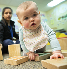 Toddler plays with blocks as caregiver looks on