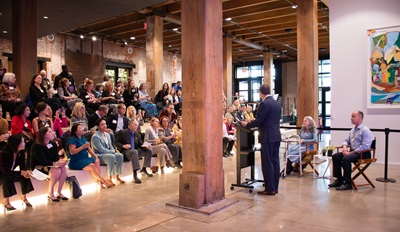 A man at a podium speaks in front of a  seated crowd