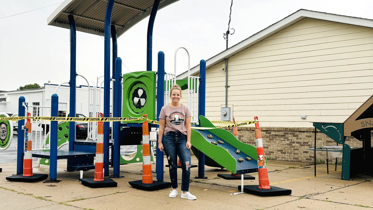 A woman stands in front of a small playground outside