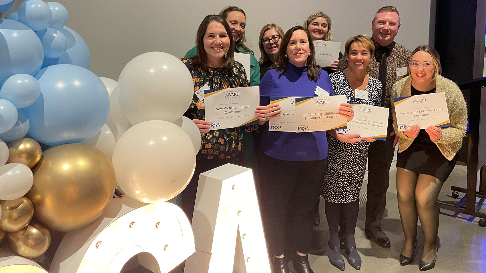 Eight people standing with award certificates at an event