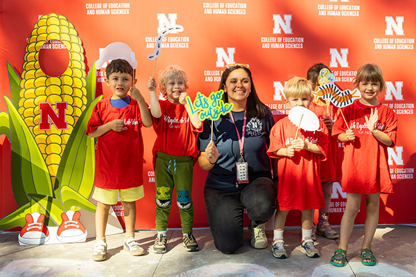 Five young children and a teacher standing in front of a red University of Nebraska backdrop
