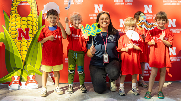 Five young children and a teacher standing in front of a red University of Nebraska backdrop
