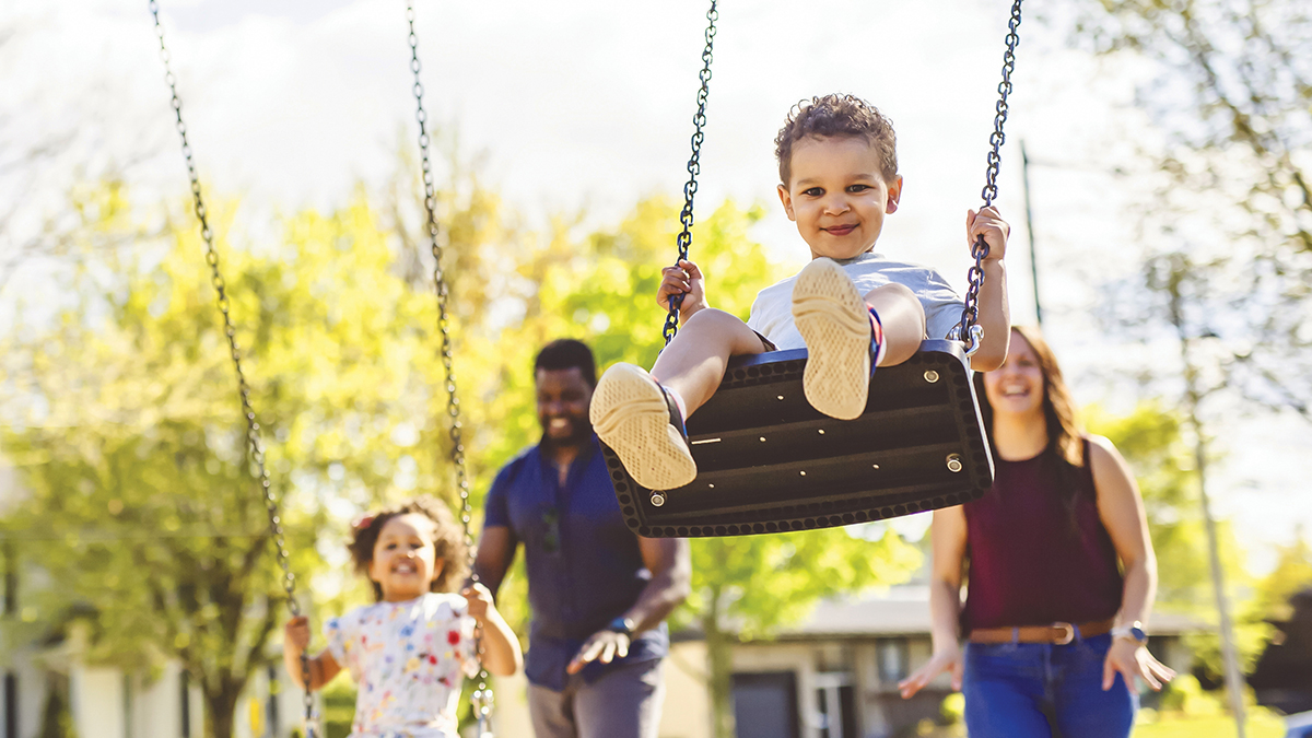 Two children with two adults behind them on a swingset