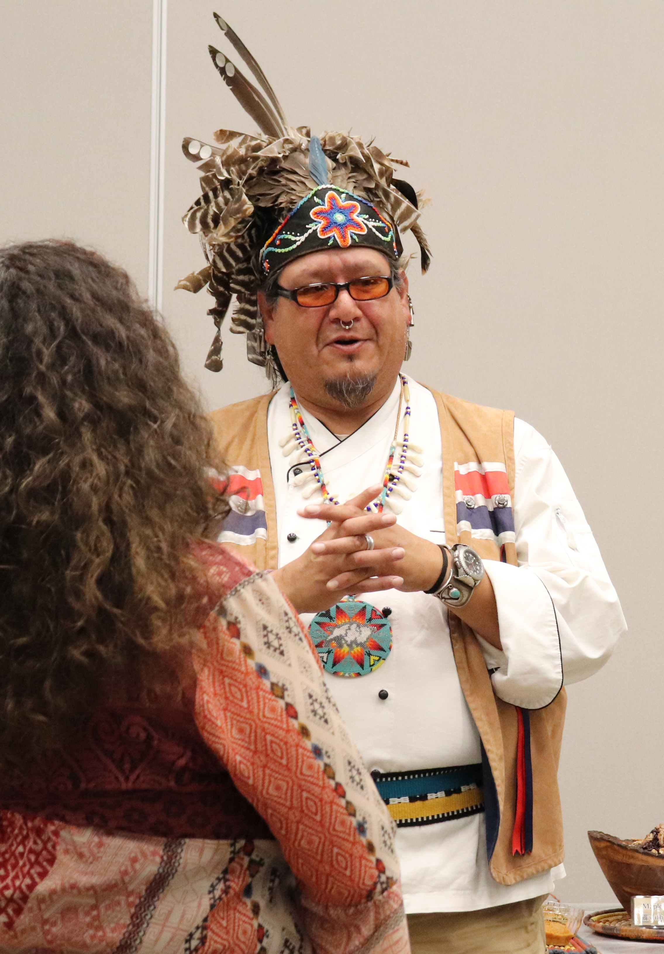 A man in a Native American headdress addresses a room