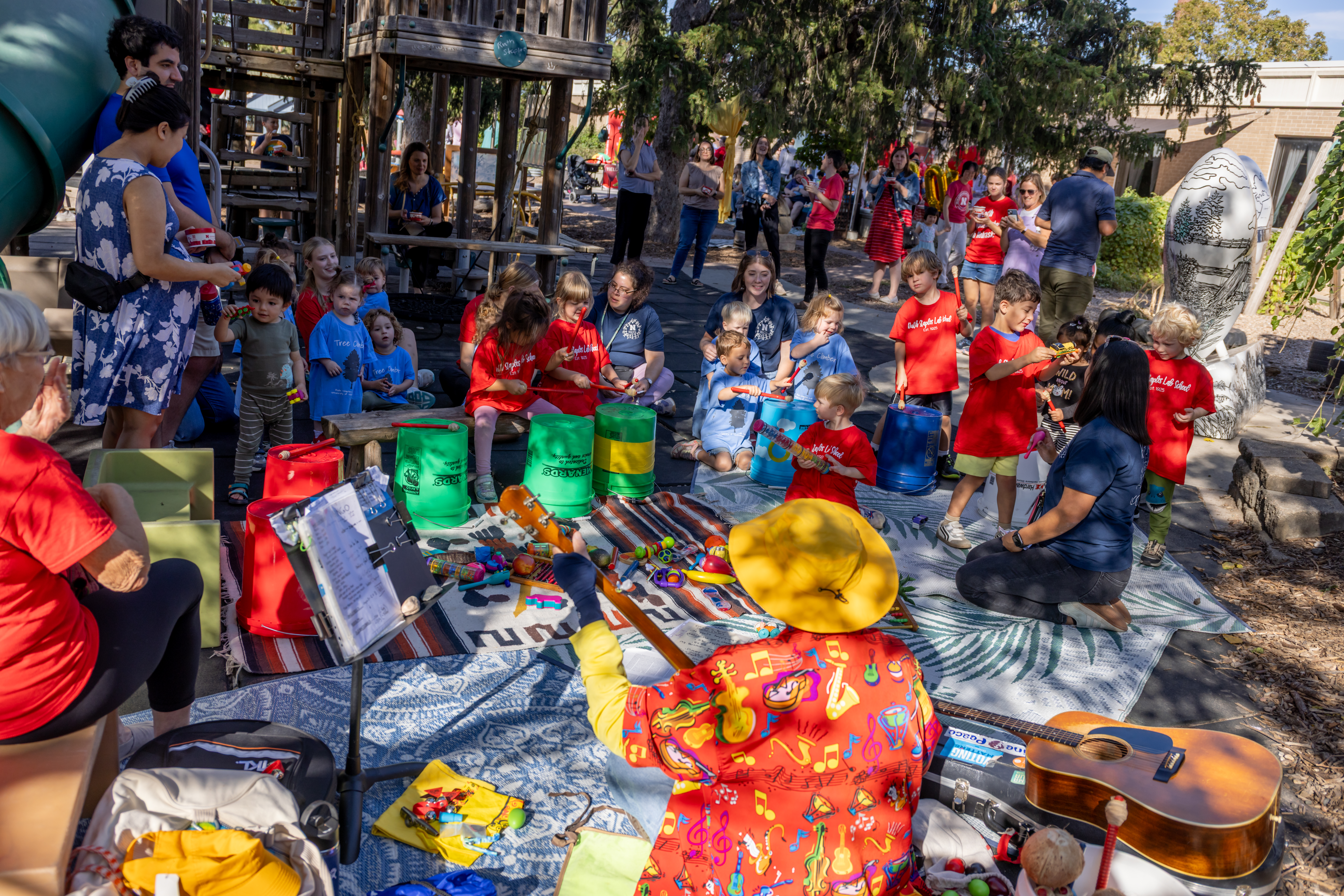 Young children and teachers create a drum circle in a play space outside
