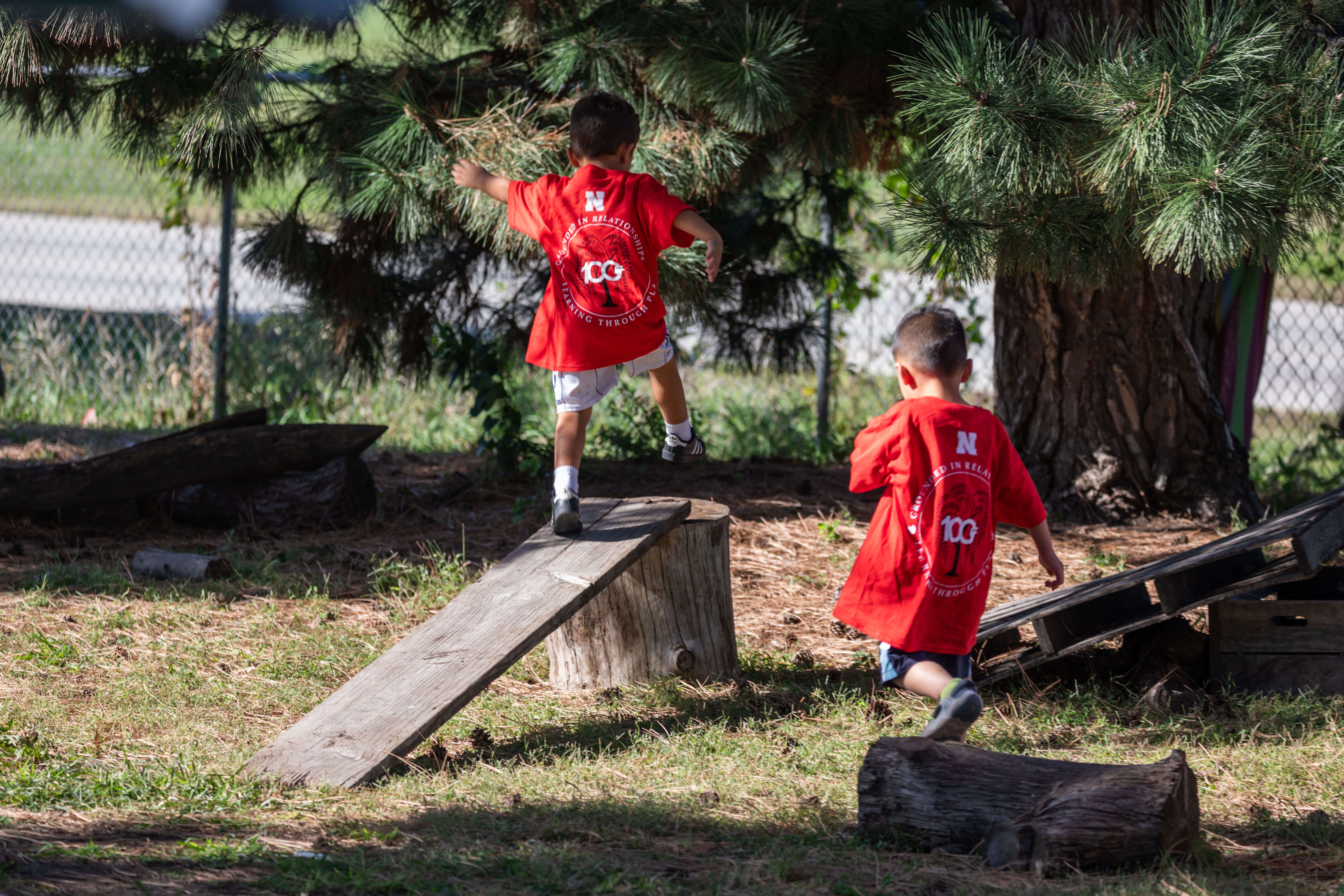 Two young children jump on stumps in an outdoor play area at the Ruth Staples Child Development Lab