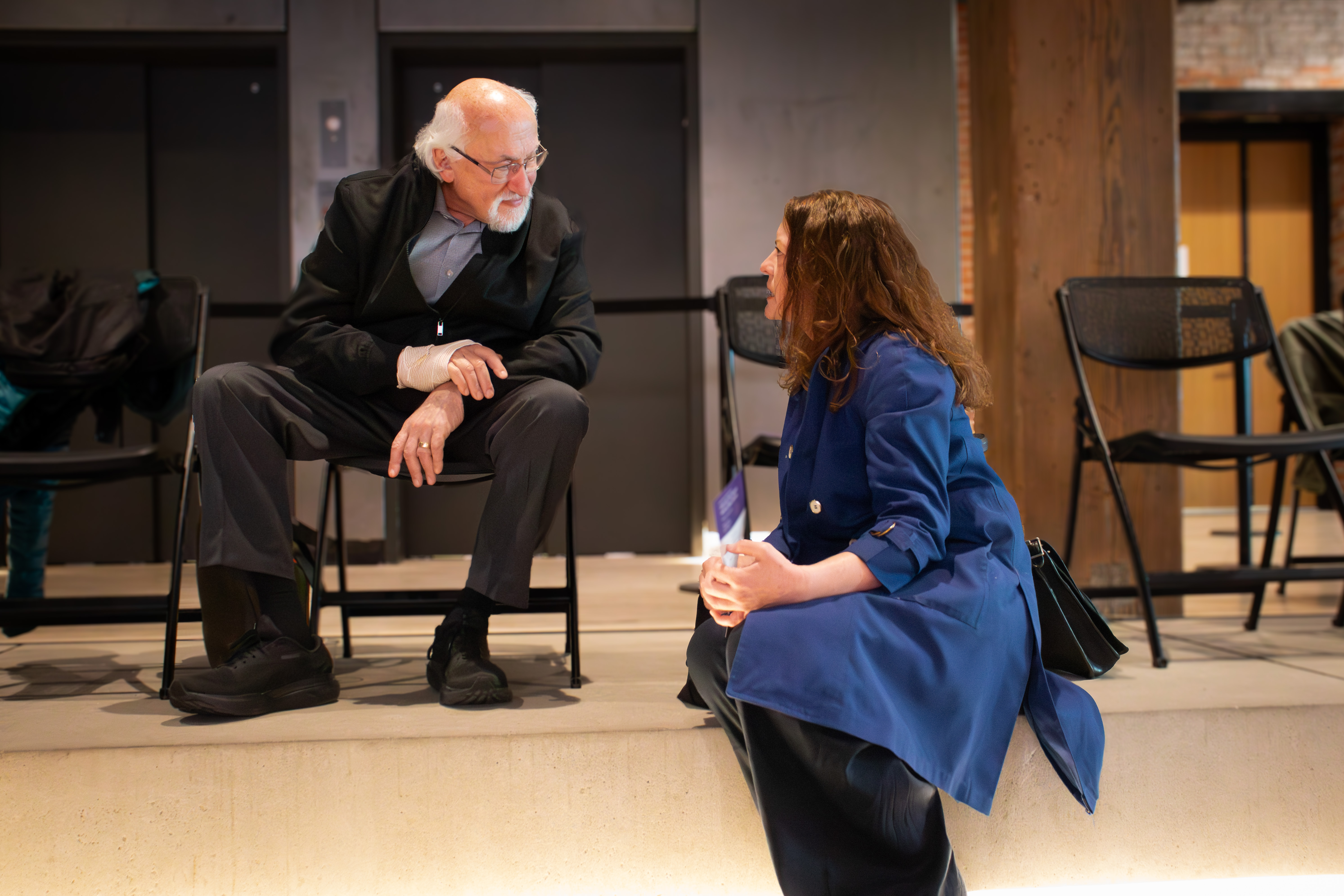 A man and woman, seated, talking to each other