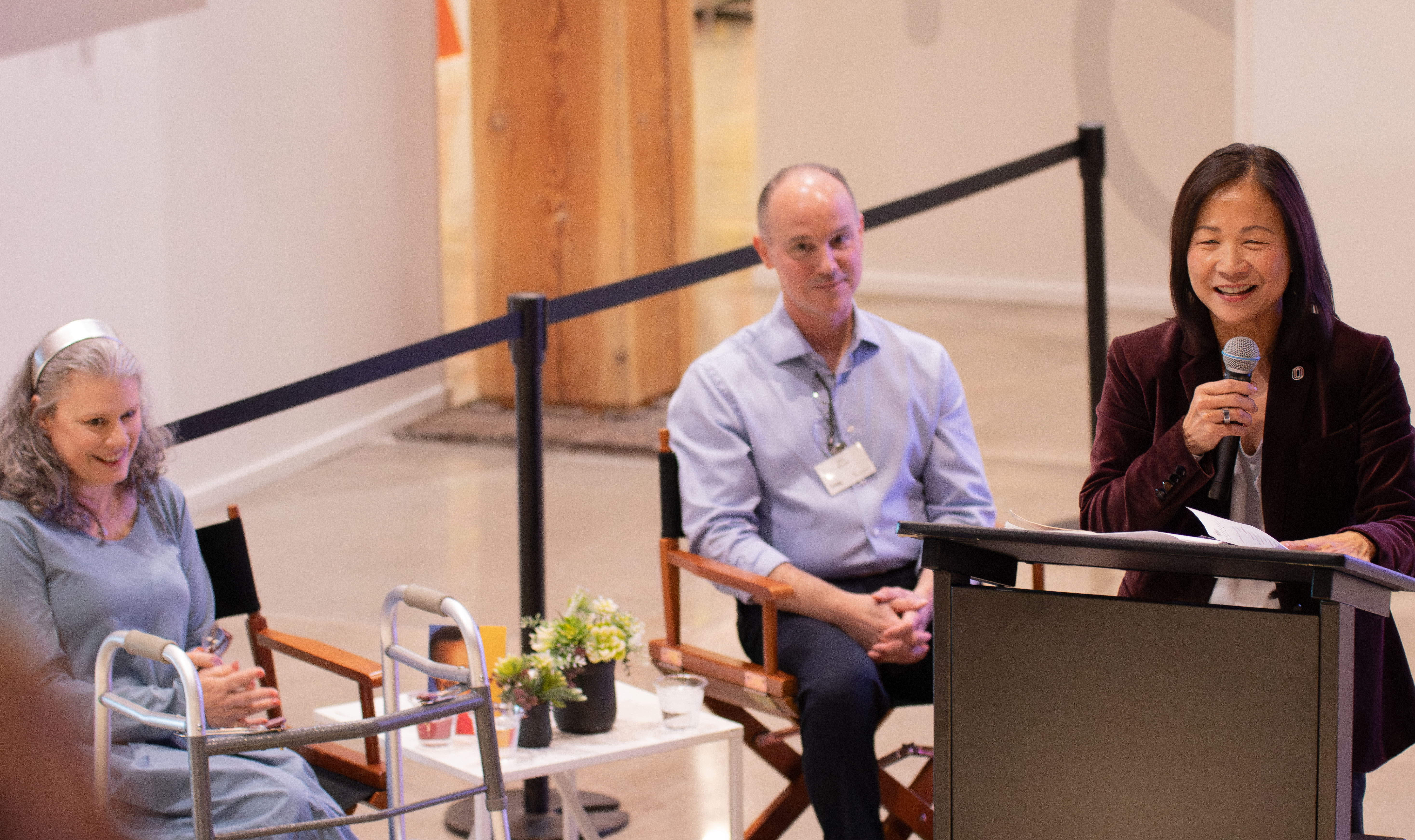 University of Nebraska at Omaha Chancellor Joanne Li speaks at a podium as Debora and Aron Wisneski look on