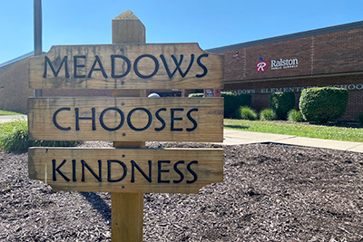 An exterior shot of Meadows Elementary School in Ralston, Neb., with a wooden sign that says, "Meadows Chooses Kindness" 