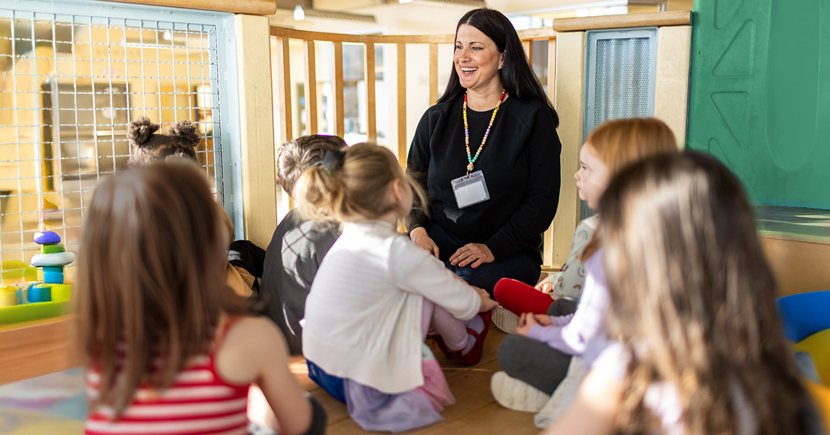 A child care provider surrounded by several preschool-age children