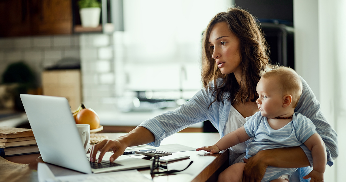 A woman holding a baby sits at a computer 