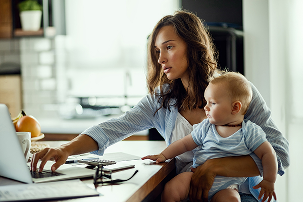 Photo of a woman at a laptop holding a baby
