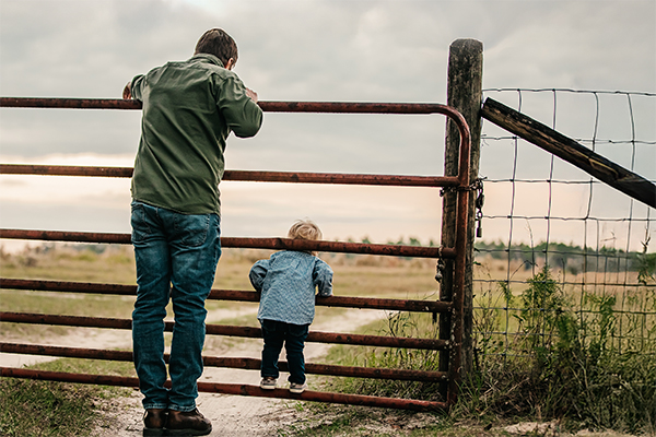 Image of a man and a young child on a farm gate 
