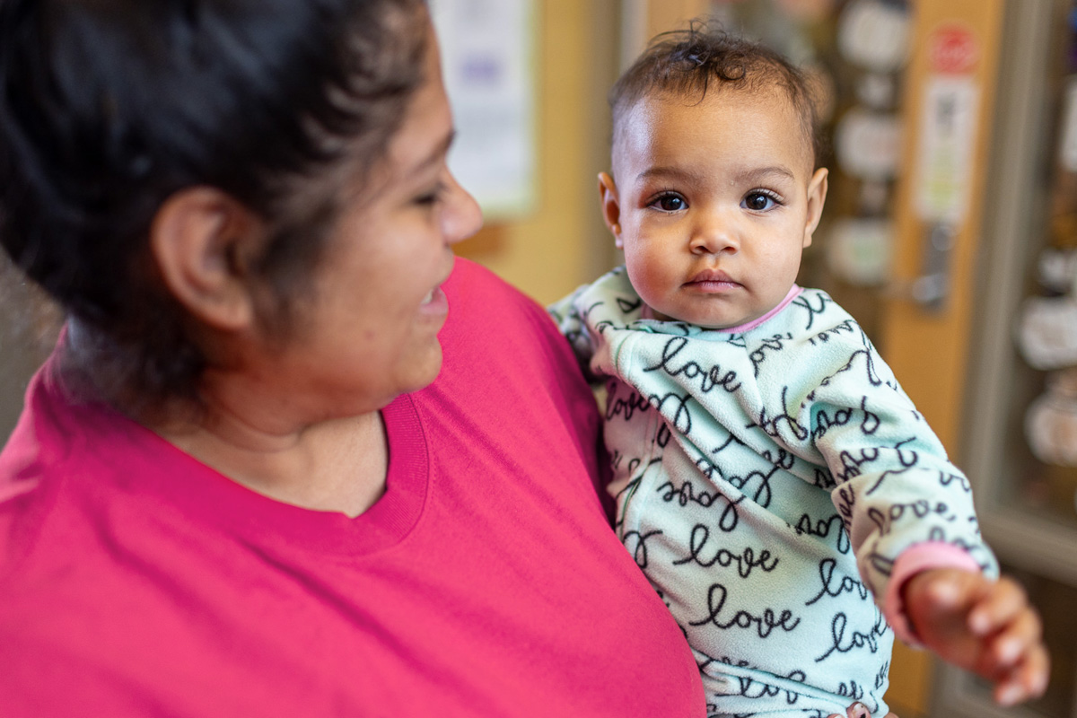 An image of a woman in a pink shirt holding a baby