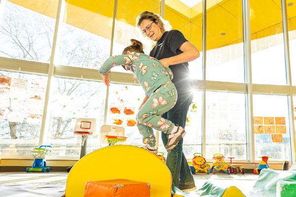 A young child jumps with a child care provider