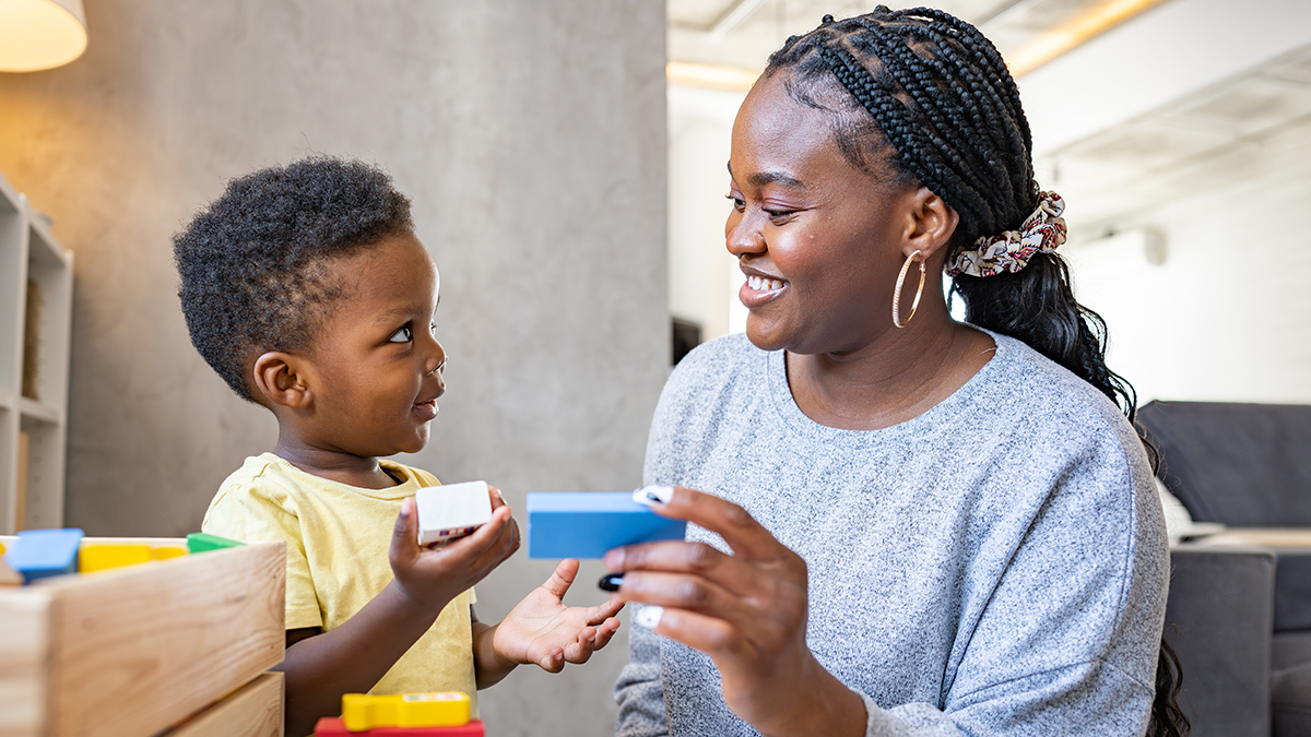 A child care provider and a young child play with blocks together