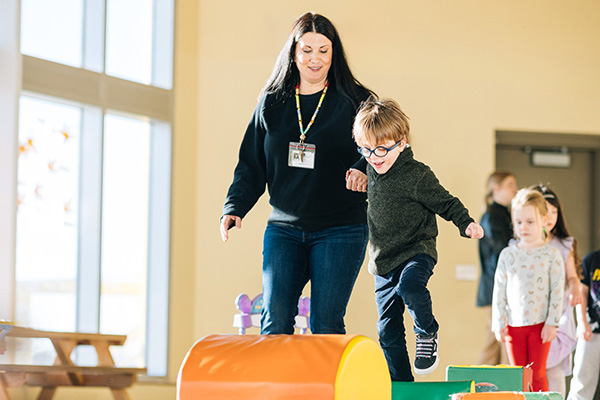 Photo of an early childhood teacher helping a young child jump