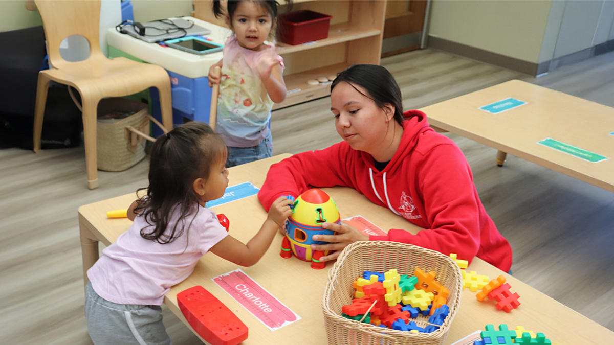 Child care provider plays at a table with a toddler