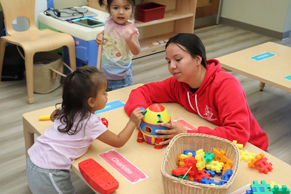 A child care provider plays at a table with a toddler