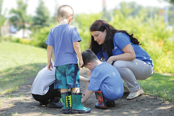 A teacher kneeling with three young children outside 