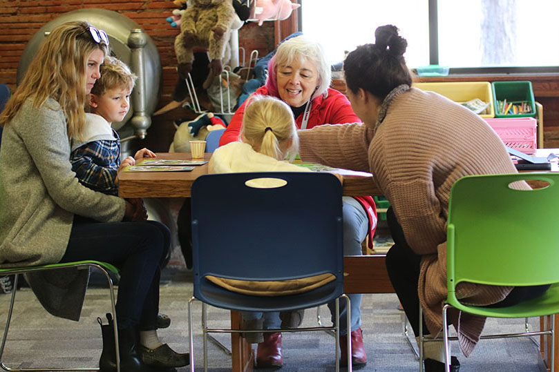 Parents, an early educator, and young children play games together at a table in a public library