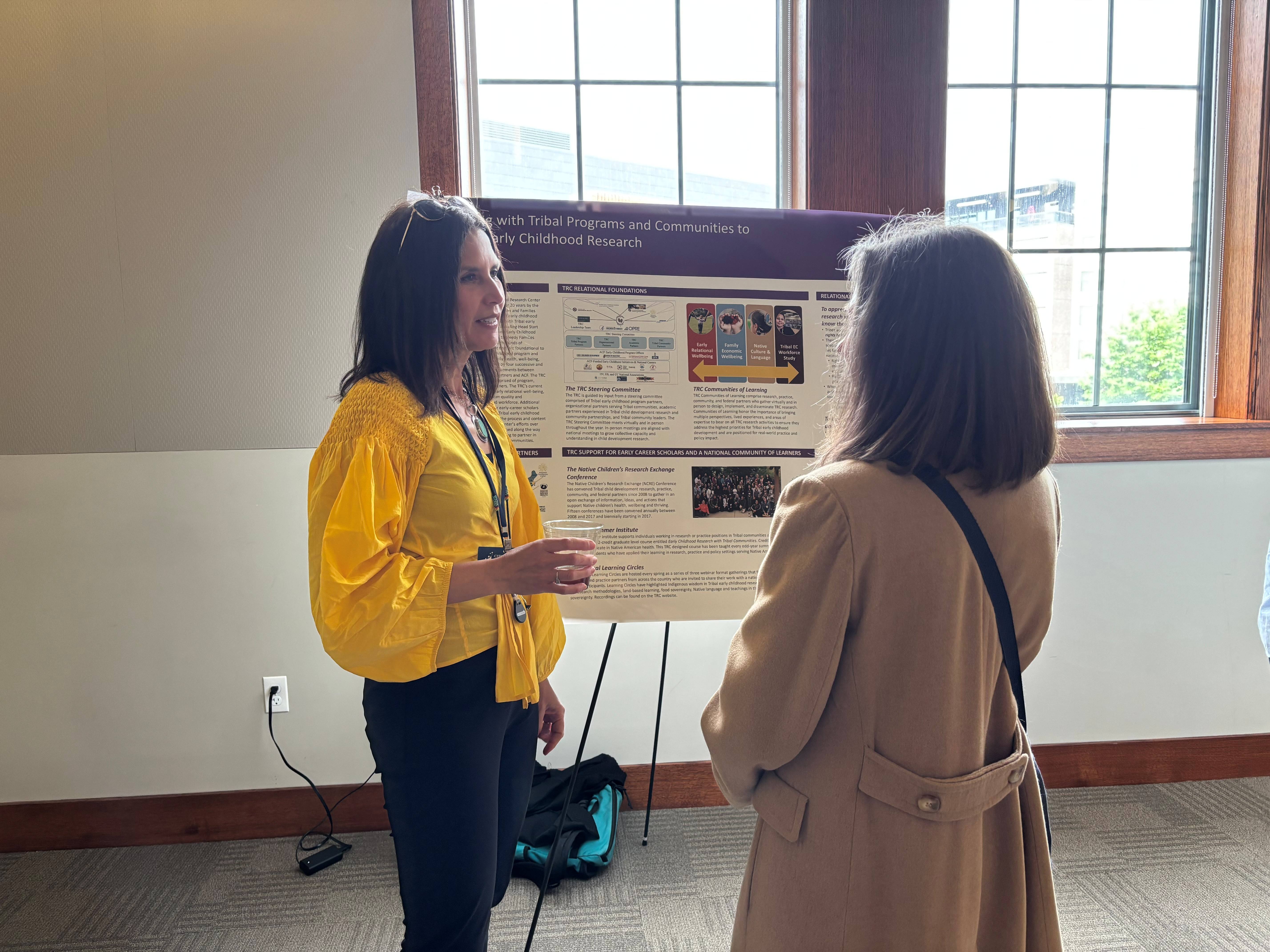 Michelle Sarche, the Buffett Institute's senior director of Tribal research, policy, and partnerships, speaks in front of her research poster with UNL Community Chair Julia Torquati. 