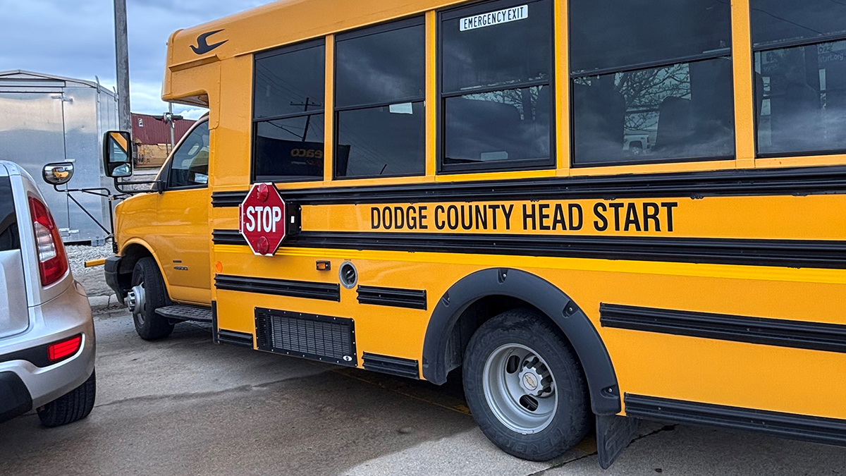 Yellow school bus parked at a curb with a red stop sign extended and the text "DODGE COUNTY HEAD START" on its side.