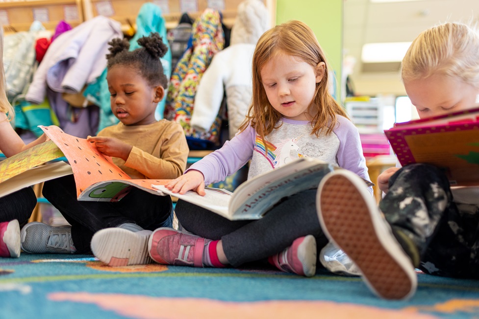 Three children sit on a carpet reading