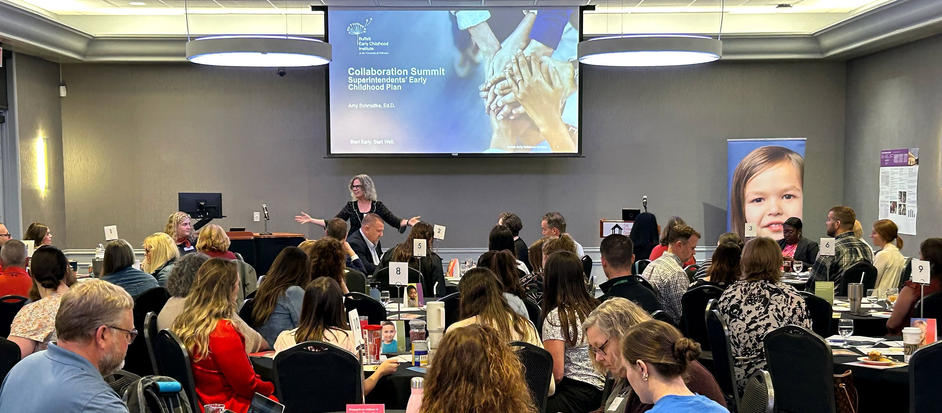 Presenter Amy Schmidtke from the Buffett Early Childhood Institute speaks to a seated audience at a Superintendents' Early Childhood Plan event, with a projected slide titled “Collaboration Summit: Superintendents’ Early Childhood Plan” overhead.