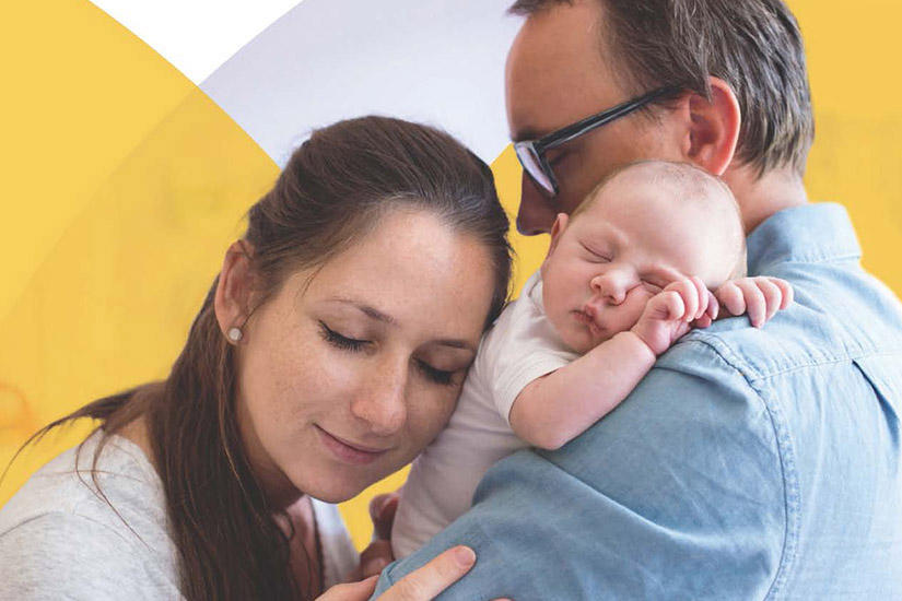 Parents cuddle their sleeping newborn baby in a close, tender embrace.