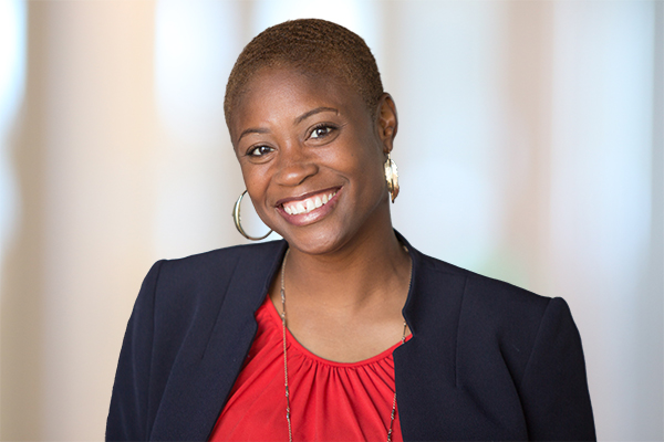 Smiling woman in a navy blazer and red top, shown in a professional headshot with a blurred background.