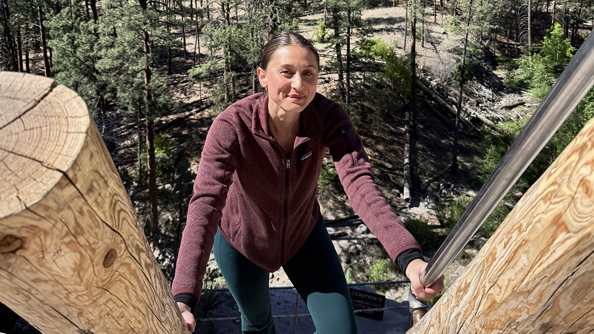 Fulbright Scholar Alexandra Gregory climbs an outdoor staircase between large wooden posts, with a forested landscape below.