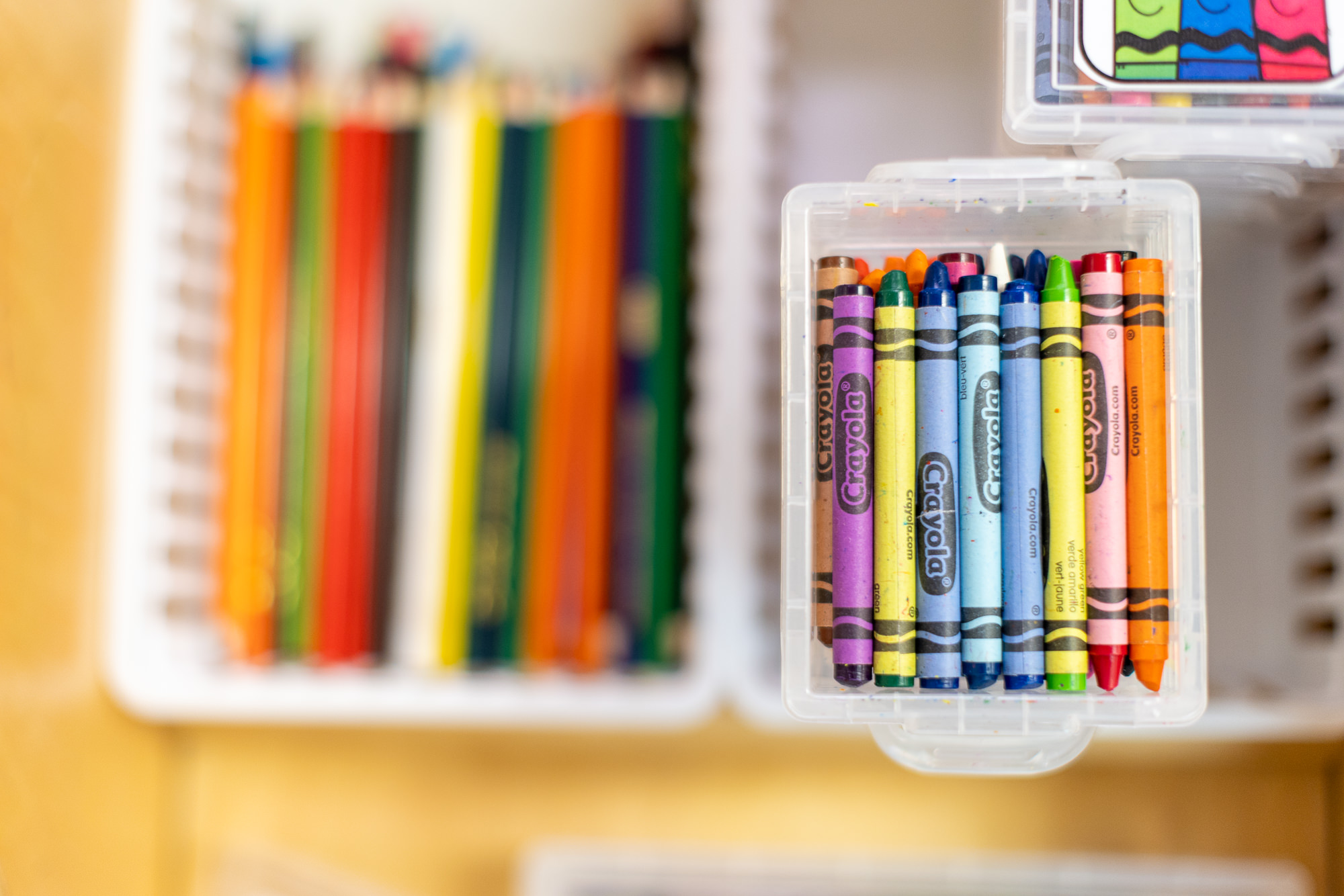Open plastic case filled with colorful crayons, with blurred colored pencils in the background.
